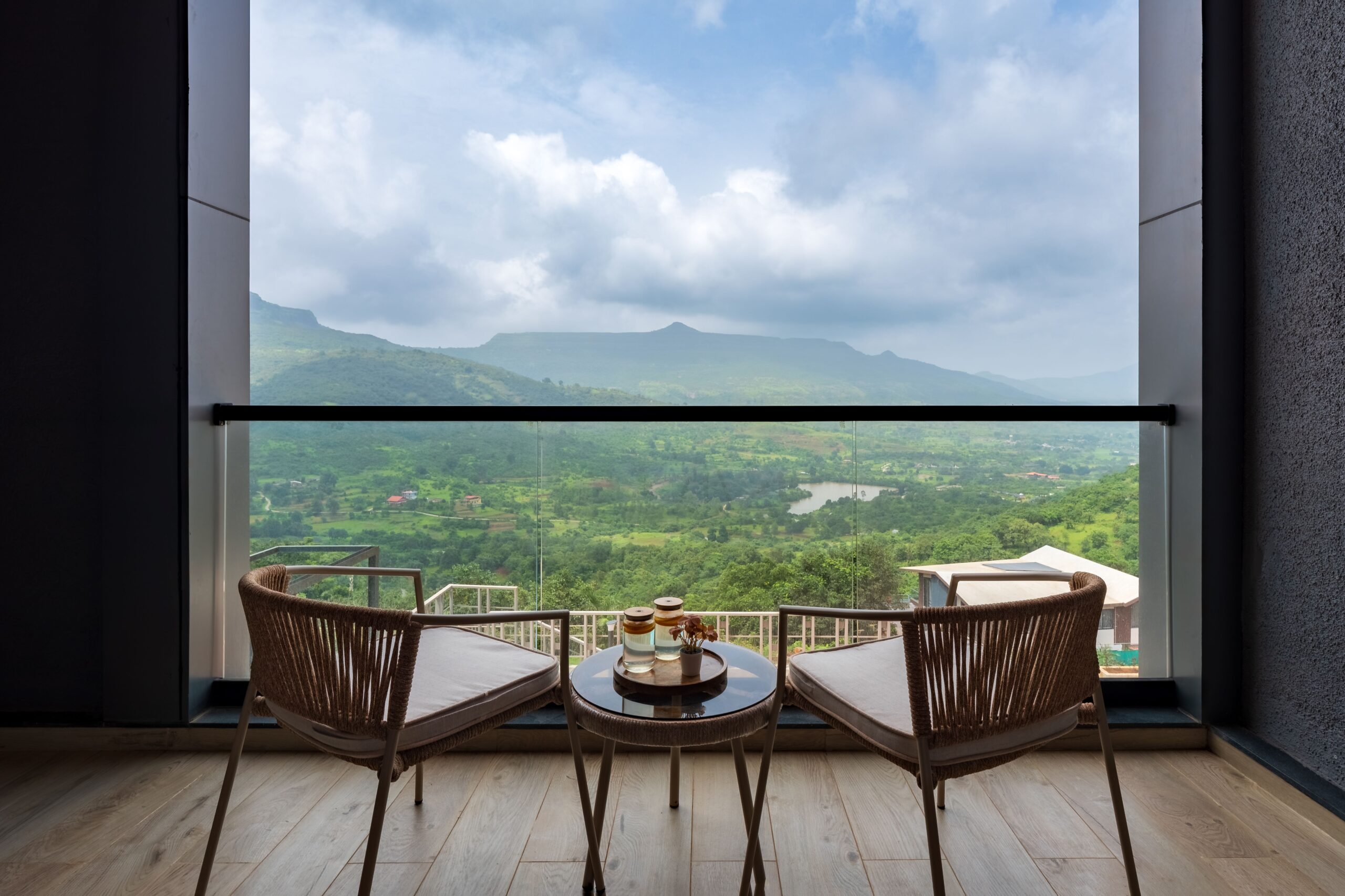 Relaxing balcony view of lush mountains and cloudy sky with two chairs and a table.